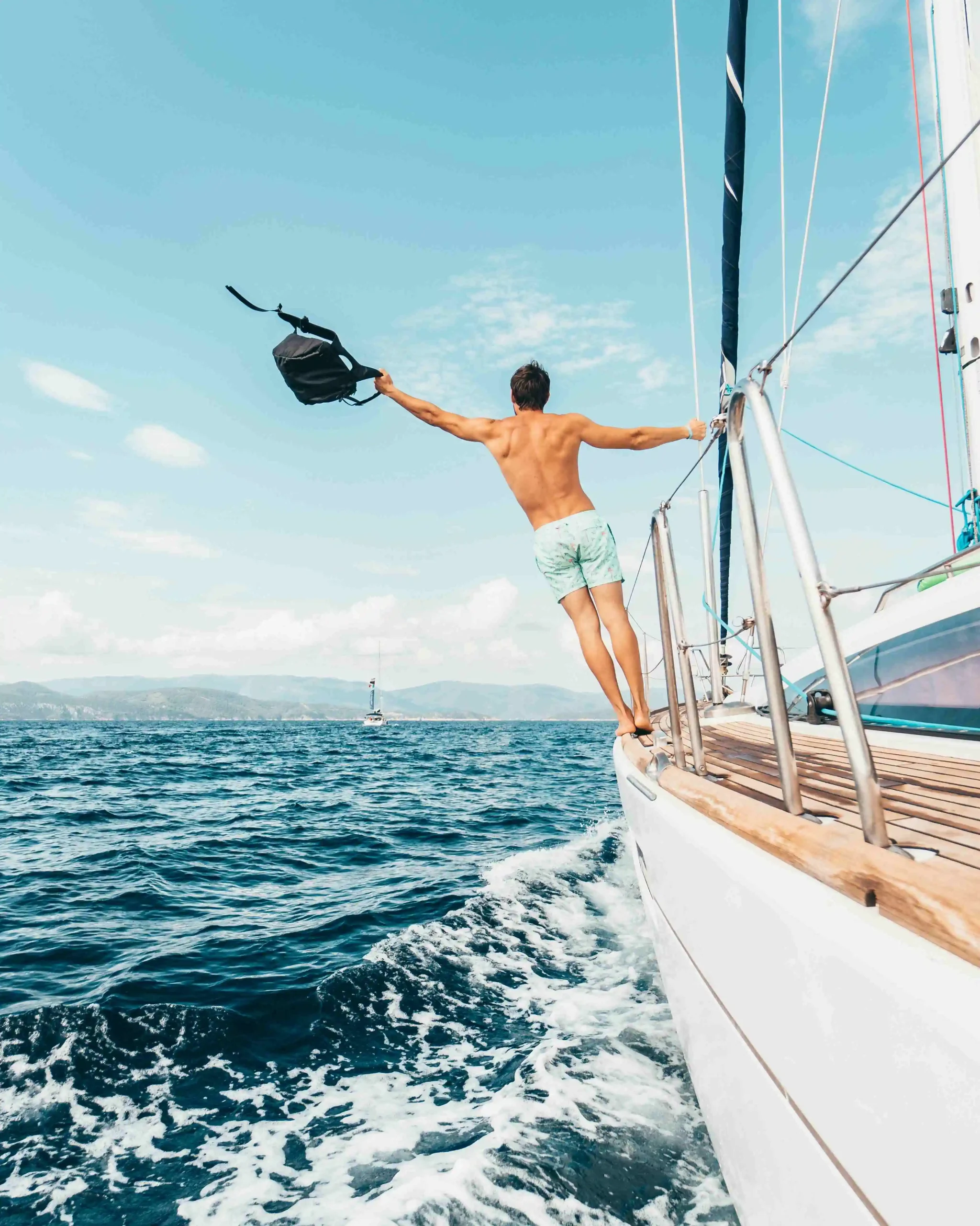 Man standing on sailboat edge over blue ocean for lifestyle editorial