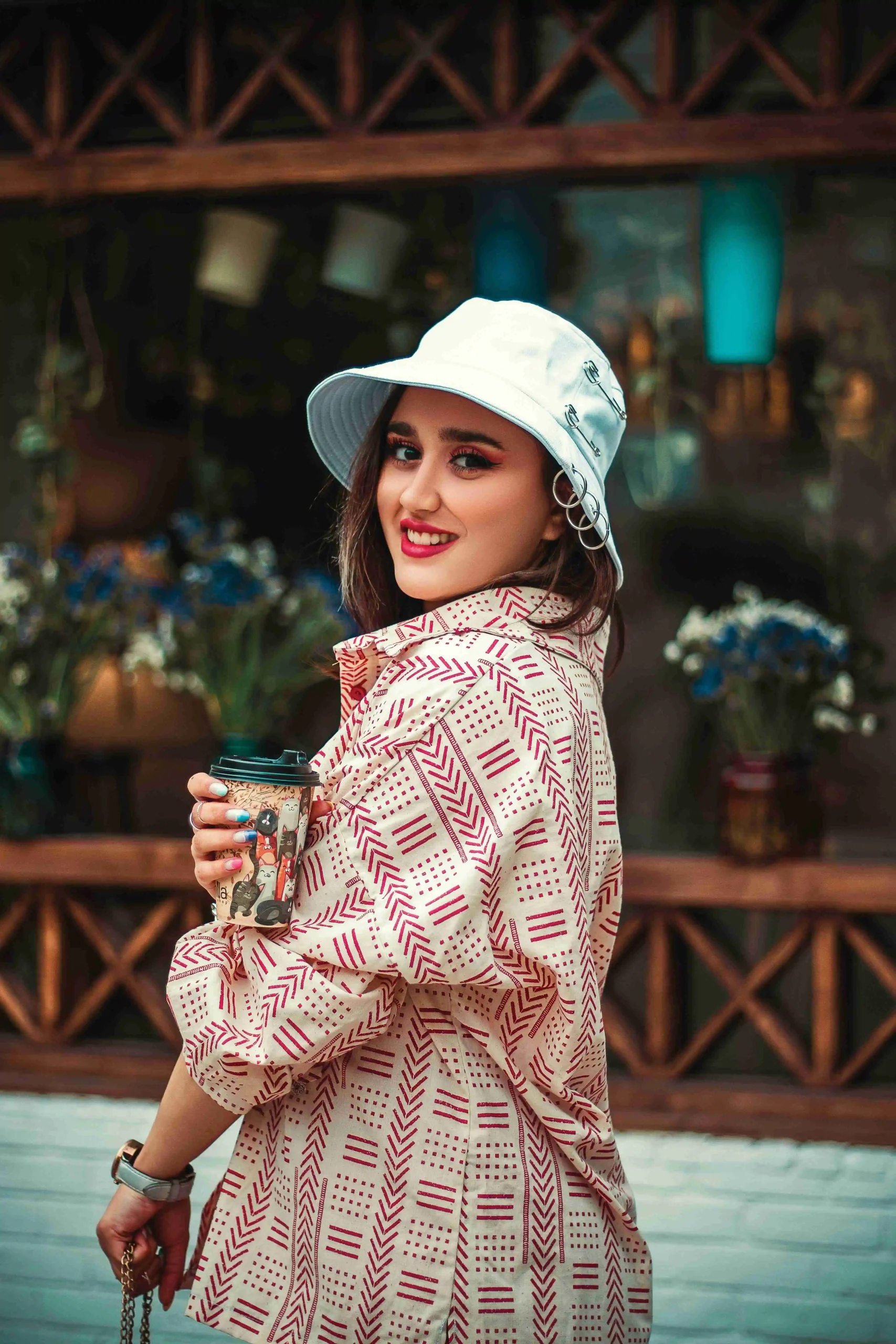 Stylish woman in bucket hat holding coffee cup at flower shop