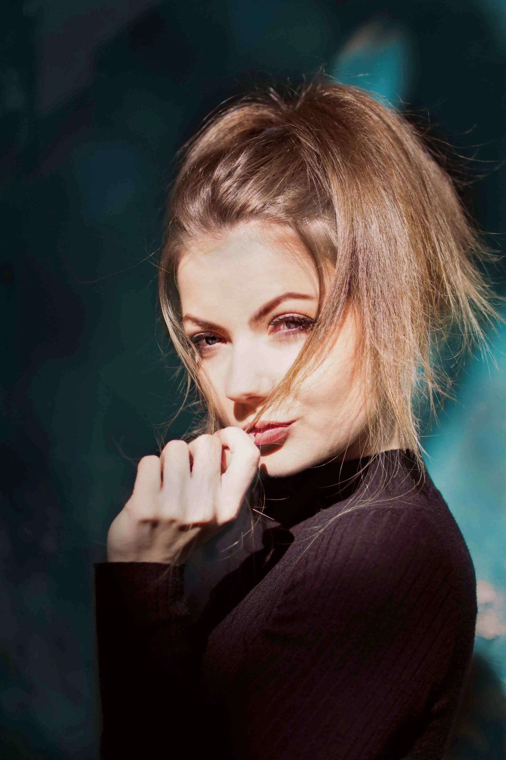 Close up portrait of woman in black turtleneck with sunlit hair for fashion editorial